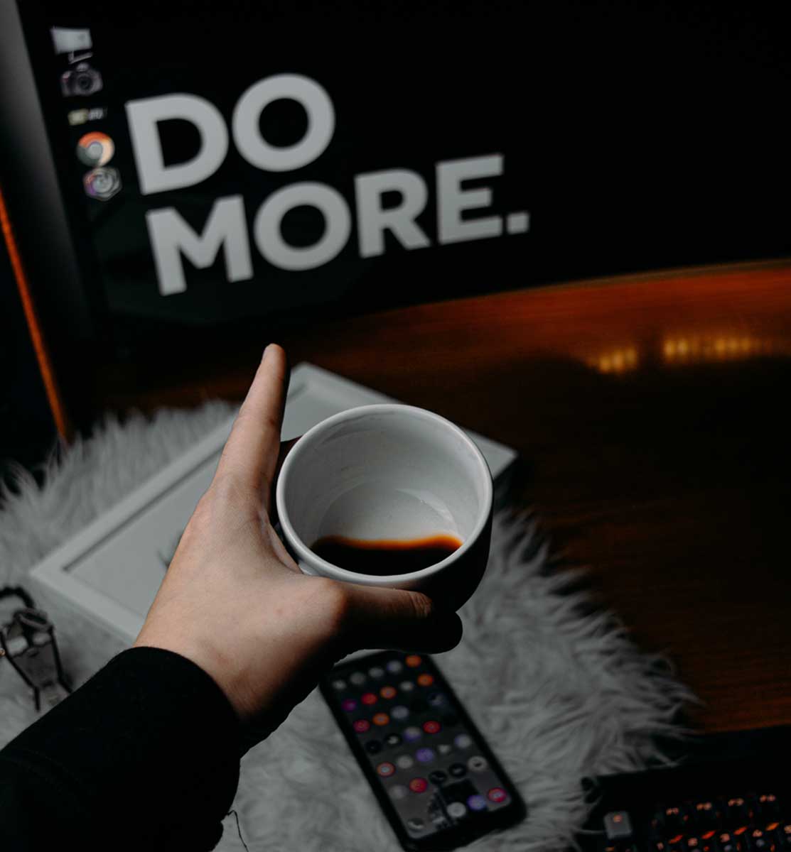 Ein Angestellter mit Kaffetasse in der Hand, auf dem Bildschirm steht: do more