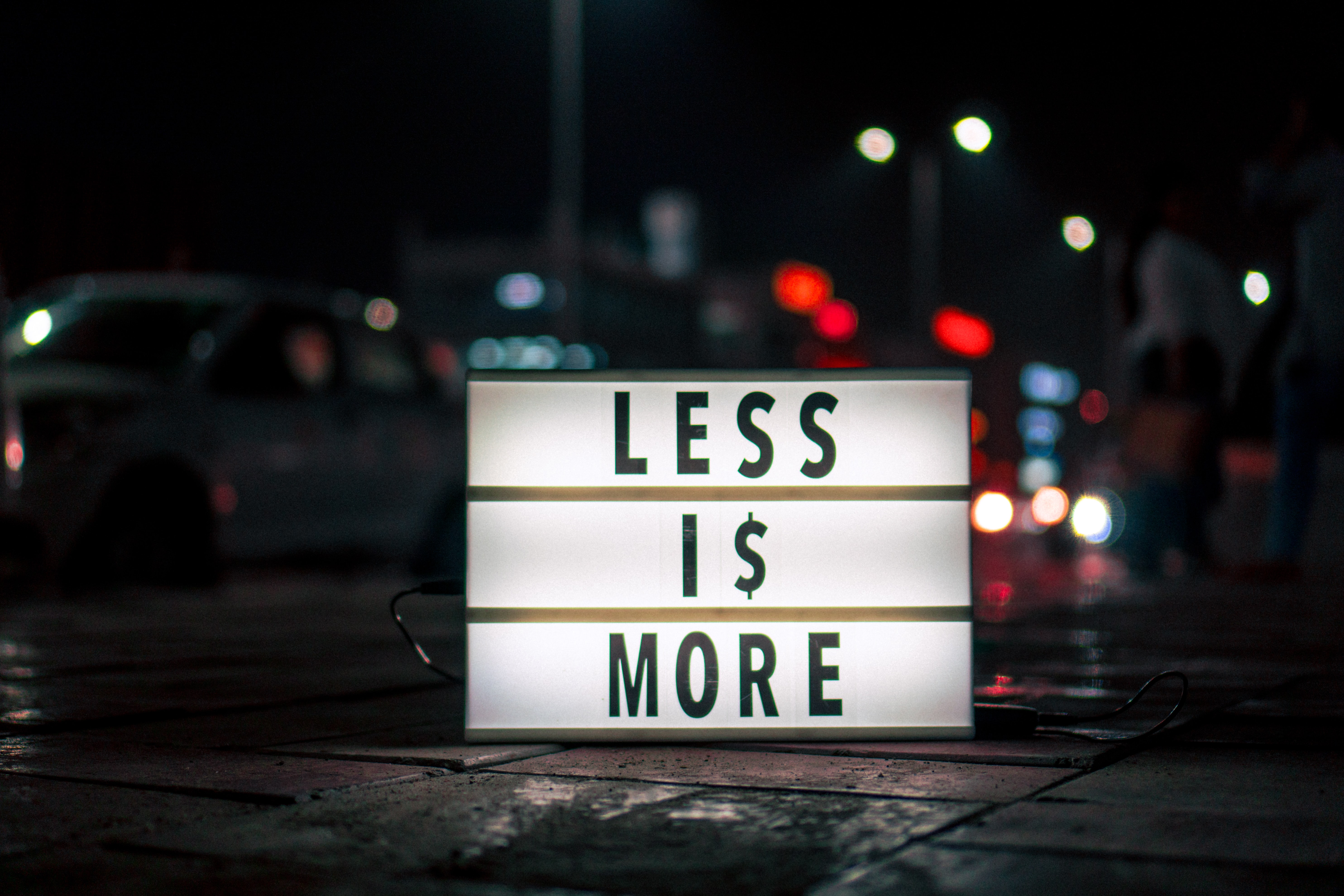 Foto von einem Leuchtschild nachts auf offener Straße. Darauf steht: "less is more".